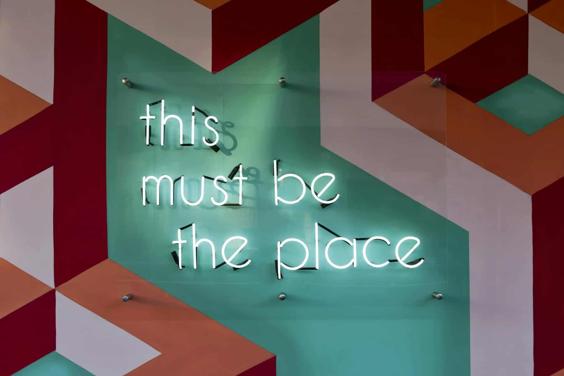 Colorful geometric wall featuring a glowing neon sign with an inspirational quote.