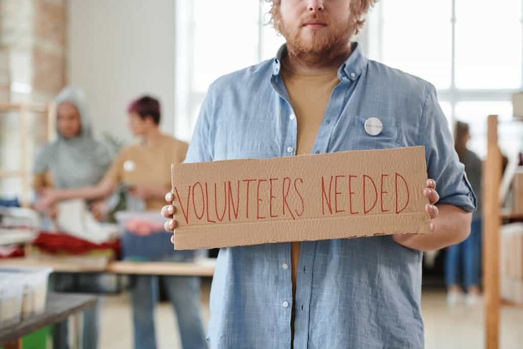 Man Holding a Sign Saying Volunteers Needed
